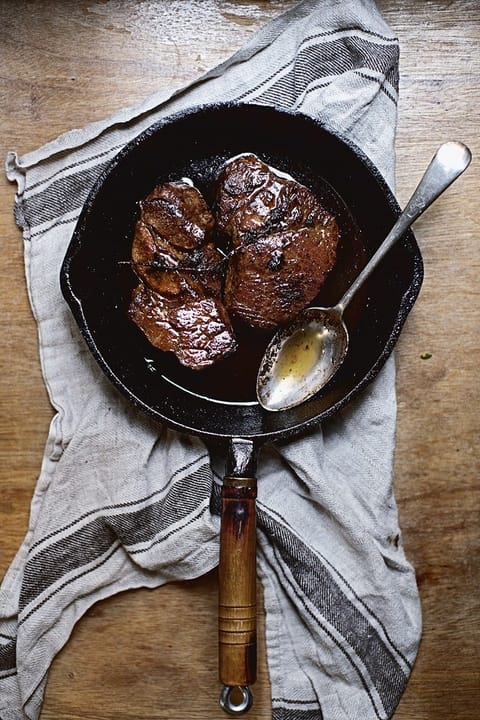 Pan-fried pork shoulder steaks in a cast-iron skillet