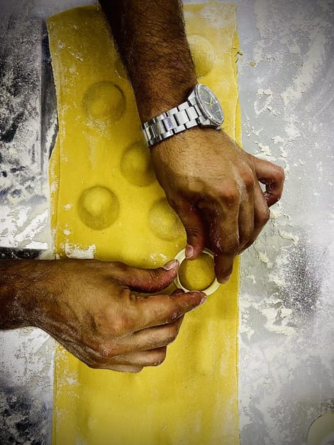 Hands pressing filling into ravioli on a sheet of fresh yellow pasta