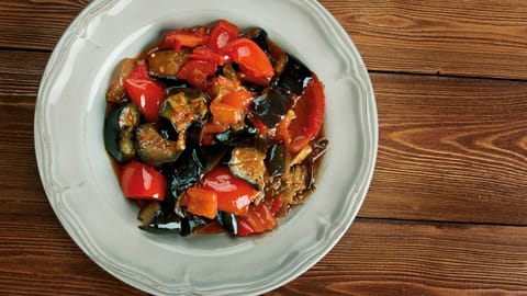 Caponata of aubergine and red pepper in a white bowl on a wooden table