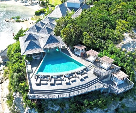 Aerial view of Riva: the curved pool, daybeds and thatched cabanas on a deck above the bay