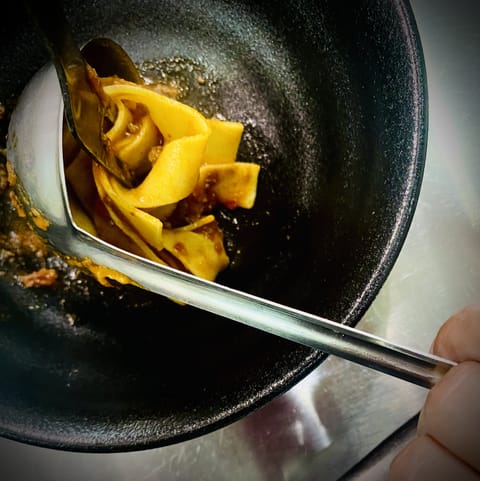 Ribbons of pappardelle being lifted out of a dark pan