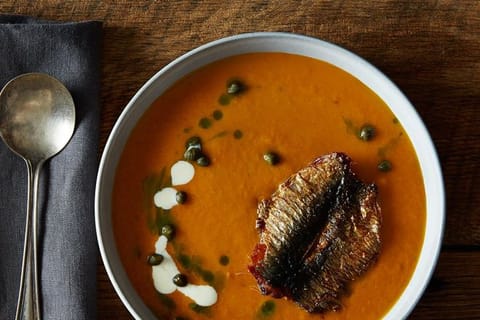 Tomato soup with capers, swirls of cream and a fried sardine