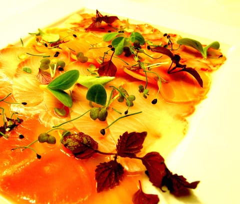 Thin slices of raw fish scattered with herbs and red leaves